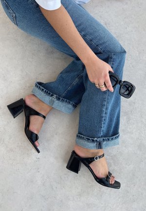 Zwarte gepatineerde leren sandalen met blokhak, een brede band, een verstelbare enkelgesp en een peeptoe-ontwerp. Gecombineerd met opgerolde spijkerbroeken.