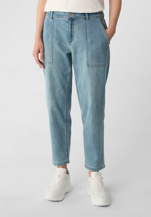Light blue denim trousers with a relaxed fit, featuring two large front pockets and rolled hems; paired with white sneakers.