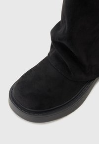 Zwarte suede laars met een ronde neus, platte zool en subtiele naaddetails. Het bovenmateriaal heeft een zachte textuur.