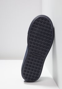 Sohle eines dunkelblauen Puma-Schuhs mit einem strukturierten Grip-Muster und dem Puma-Logo, zentriert auf einer schlichten weißen Fläche in der Nähe der Wände.