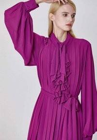Robe fuchsia à manches longues avec plis, devant volants et ceinture à nouer. Comprend des poignets boutonnés et un tissu doux et fluide.