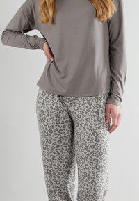 Grå långärmad topp kombinerad med ljusgrå byxor som har ett mönster av mörkgrå leopardfläckar. Mjuk tygkvalitet med en avslappnad passform och utan synlig hårdvara.