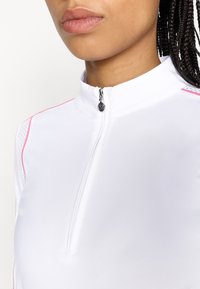 Valkoinen vetoketjullinen urheilupaita, jossa on korkea kaulus ja vaaleanpunaiset ompeleet. Varustettu pienellä vetoketjun vedolla ja hengittävillä verkko-osiolla sivuilla.