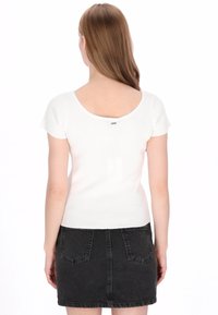 Witte geribbelde top met korte mouwen en een diepe rug, gecombineerd met een donkergrijze denim rok met achterzakken en een zoom boven de knie.