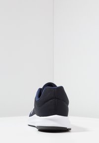 Baskets de sport bleu marine avec une tige en mesh texturé, un talon rembourré et une semelle intermédiaire blanche, dotées d'une semelle extérieure en caoutchouc noir pour l'adhérence.