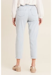 Lichtblauwe,opgerolde jeans met een relaxte pasvorm, voorzien van twee achterzakken en een elastische tailleband, gecombineerd met tan schoenen.