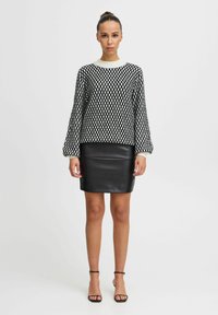 Maglione a righe in bianco e nero con scollo rotondo, abbinato a una gonna in pelle nera aderente e sandali neri con cinturino.