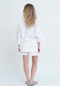 Tunic bianca testurizzata con maniche ampie, abbinata a pantaloni corti bianchi coordinati. L'outfit presenta una vestibilità rilassata e un design casual.