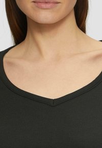 Schwarzes, geripptes Oberteil mit tiefem V-Ausschnitt und strukturiertem Stoff; Details umfassen eine subtile Naht am Ausschnitt und eine figurbetonte Silhouette.