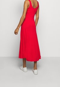 Czerwona, bezrękawnikowa sukienka midi wykonana z miękkiego materiału, z rozkloszowanym dołem i okrągłym dekoltem z tyłu. Noszona z białymi trampkami.