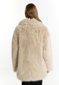 Beige faux fur frakke med en fyldig tekstur, bred krave og løs pasform. Har et markant shaggy udseende og lange ærmer.