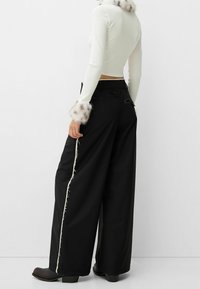 Black wide-leg pants with frayed white side seams, paired with a fitted white top featuring fuzzy cuffs. Black ankle boots complete the look.