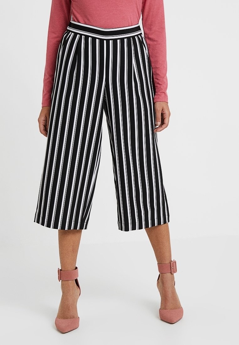 Culottes rayés noir et blanc avec une taille haute, associées à un haut rose à manches longues et des escarpins roses à brides de cheville.