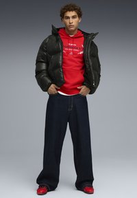 Sorte pufferjakke med en blank overflade, rød hættetrøje med hvid grafisk tryk, løse mørkeblå jeans og røde træningssko.