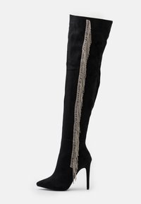 Bota negra por encima de la rodilla hecha de ante, con tacón de aguja y un cascada vertical de rhinestones plateados a lo largo del costado.
