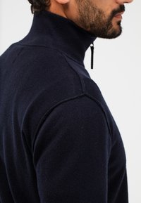 Marinefarbener Rollkragenpullover aus weichem Strickstoff, mit hohem Kragen und Reißverschluss. Weiche Textur mit körperbetonter Silhouette.