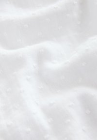 Tessuto bianco con una superficie morbida e strutturata caratterizzata da piccoli pois in rilievo distribuiti su tutta la superficie, creando un aspetto delicato e arioso.