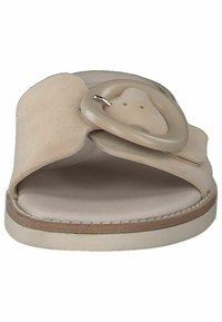 Beige slip-on sandal i mocka och slät läder. Har ett brett band och en cirkulär hårdvarudetalj i mitten. Platt sula.