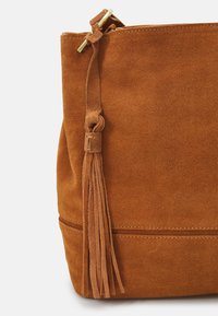 Suede taske i en rig brun farve med en flad form. Har en frynseaccent og stikninger langs bunden.