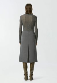 Siva suknja prilagođena uz tijelo s prorezom straga, uparena s uskim, metaliziranim pletenim topom. Model nosi smeđe čizme do koljena. Jednostavan, elegantan dizajn.