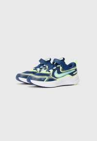 Des chaussures de sport bleu marine et vert fluo présentent une tige en mesh, un col rembourré, une sangle ajustable et une semelle blanche avec une traction texturée.