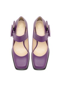 Chaussures en cuir violettes avec un bout carré, une bride de cheville et un grand accent circulaire. L'intérieur est doté d'une doublure beige douce. Semelle noire plate.