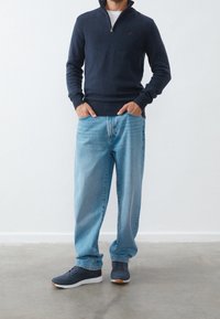 Granatowy sweter z zamkiem, jasnoniebieskie dżinsy, szare buty sportowe z białymi podeszwami. Luźny krój, casualowy design, teksturowany splot i denimu.