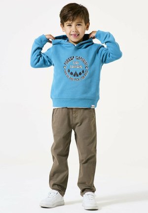 Sweat à capuche bleu avec un graphique "Forêt Évasion", pantalon beige et baskets blanches. Comprend des poignets côtelés et une poche kangourou.