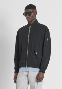Giubbotto bomber nero con zip frontale, tasche laterali e polsini elasticizzati. Presenta una tasca con zip sulla manica sinistra, realizzato in tessuto morbido.