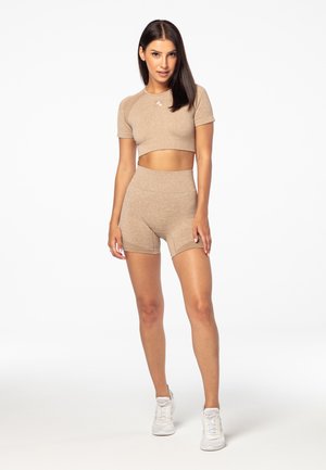 Beżowy kompletny zestaw sportowy z krótkim topem z krótkimi rękawami i szortami z wysokim stanem. Materiał wydaje się miękki o gładkiej teksturze.