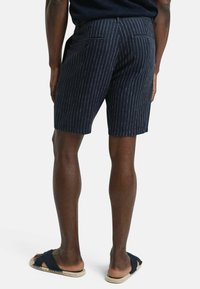 Marine gestreepte shorts met een getailleerde pasvorm, voorzien van een textuurstof, twee achterzakken en een eenvoudige tailleband. Gekocht met donkere sandalen.