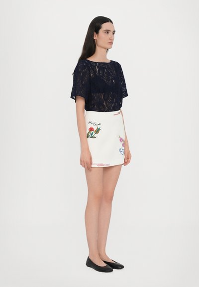 Lace navy top with short sleeves paired with a white skirt featuring floral embroidery and red accents, complemented by black flats.