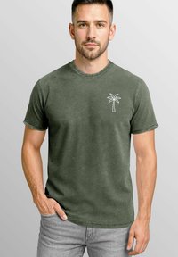 Olivgrünes T-Shirt mit kurzen Ärmeln aus einer weichen Baumwollmischung, mit einem weißen, gestickten Palmenmotiv auf der linken Brust.