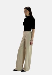 Zwarte fitted top met korte mouwen, gecombineerd met beige wijde broek, beide gemaakt van soepele stoffen. Model staat in profiel.