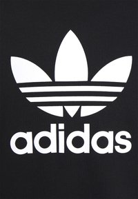 Svart tyg med en stor vit Adidas trefoil-logga ovanför ordet "adidas" i fet, versal text.