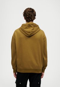 Kapuzensweatshirt aus olivgrünem Stoff mit einer lockeren Passform, gerippten Bündchen und einem Bündchen an der Taille. Die strukturierte Fläche sorgt für Tiefe.