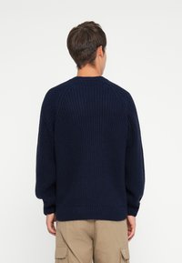 Navy knitted sweater with a textured pattern, round neckline, raglan sleeves, and ribbed cuffs, shown from the back.