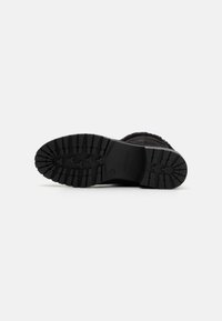 Semelle de botte noire avec une surface en caoutchouc texturé présentant de profonds sillons pour une meilleure adhérence. Marquage clair sur le côté gauche.
