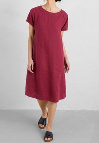 Löstsittande klänning med kort ärm i djup burgundy-linne, med rundad halsringning och sidofickor, tillsammans med svarta sydda sandaler.
