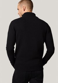 Czarny sweter z dzianiny z wysokim kołnierzem, prążkowanymi mankietami i dolnym wykończeniem. Posiada gładką teksturę i dopasowany krój.