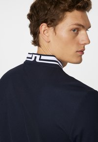 Marinblå blazer med en strukturerad passform, prydd med en krage i vit och svart rand. Slät textur och skräddarsydd design som visar en modern profil.