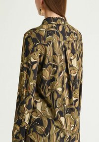 Langärmliges Hemd aus dunklem Stoff mit floralem Muster in Grün, Creme und Burgunderrot. Maßgeschneiderter Kragen mit Rückenpasse.