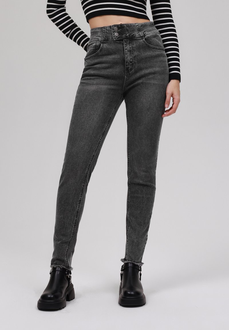 High-waisted black denim jeans with a slim fit, featuring front pockets, a button fly, and frayed hems. Paired with black ankle boots.