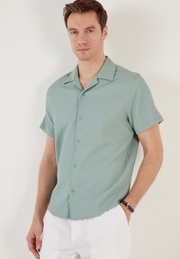 Korte mouwen, mintgroen shirt met een subtiele ribbeltextuur, knoopsluiting en een spread collar, gecombineerd met witte gestreepte broek.