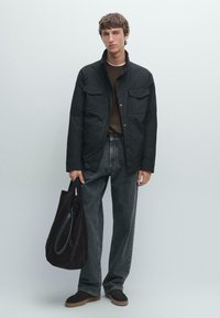 Giacca nera con due tasche frontali, tessuto texturizzato, abbinata a jeans grigio scuro e scarpe in suede marroni. Borsa a tracolla nera con texture morbida.