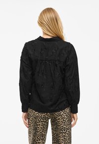 Svart blus med blomstermönster, långa ärmar och krage, tillsammans med byxor med leopardmönster. Strukturerad tyg med detaljerade accenter.