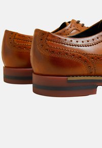 Bruine leren schoenen met brogue-details, een ronde neus en een gestapelde hak met een contrasterende zwarte streep. Glad oppervlak en gepolijste afwerking.