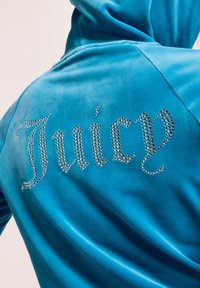 Hoodie in velour turchese con la scritta "Juicy" in strass argentati sul retro, dotato di cappuccio con coulisse e texture morbida.