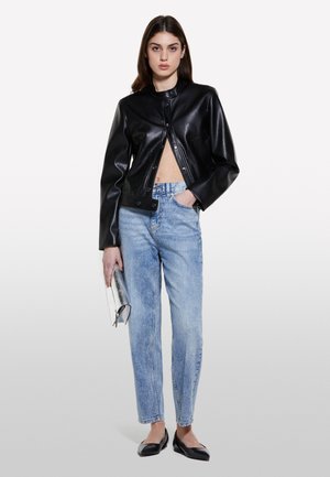 Veste en cuir noire raccourcie avec un col rond, jeans taille haute bleu clair, ballerines noires et une pochette métallique argentée.