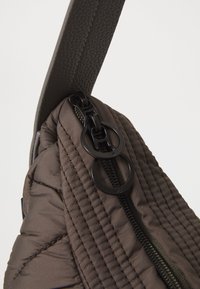Close-up of dark brown quilted fabric bag with black zipper and dual circular zipper pulls, attached to textured strap.